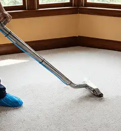 Steam carpet cleaning technician using a hot-water extraction wand on a residential carpet, wearing blue protective shoe covers Minneapolis, MN.