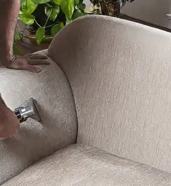 Professional upholstery cleaner deep-cleaning a fabric sofa with a handheld extraction tool and hose Minneapolis, MN.