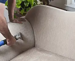 Professional upholstery cleaner deep-cleaning a fabric sofa with a handheld extraction tool and hose in Minneapolis, MN.